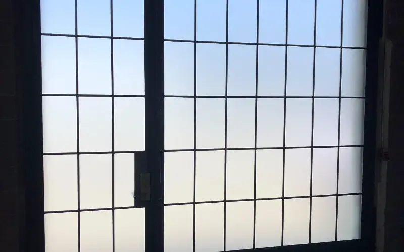 A steel grid window fully frosted, glowing with daylight but giving nothing away.
